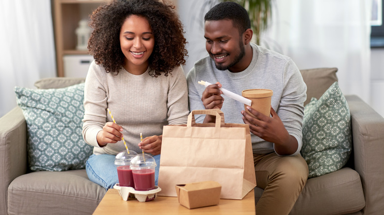 Young couple on the couch eating take-out smoothies