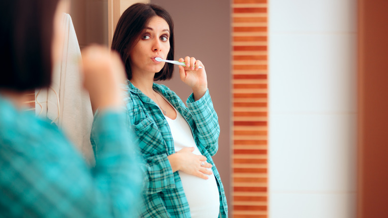 pregnant woman brushing teeth in mirror