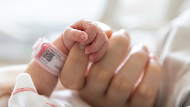 newborn baby holding mothers finger