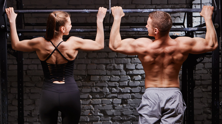 Man and woman doing chin-ups at the gym