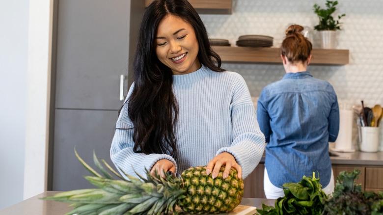 Smiling woman slicing a fresh pineapple