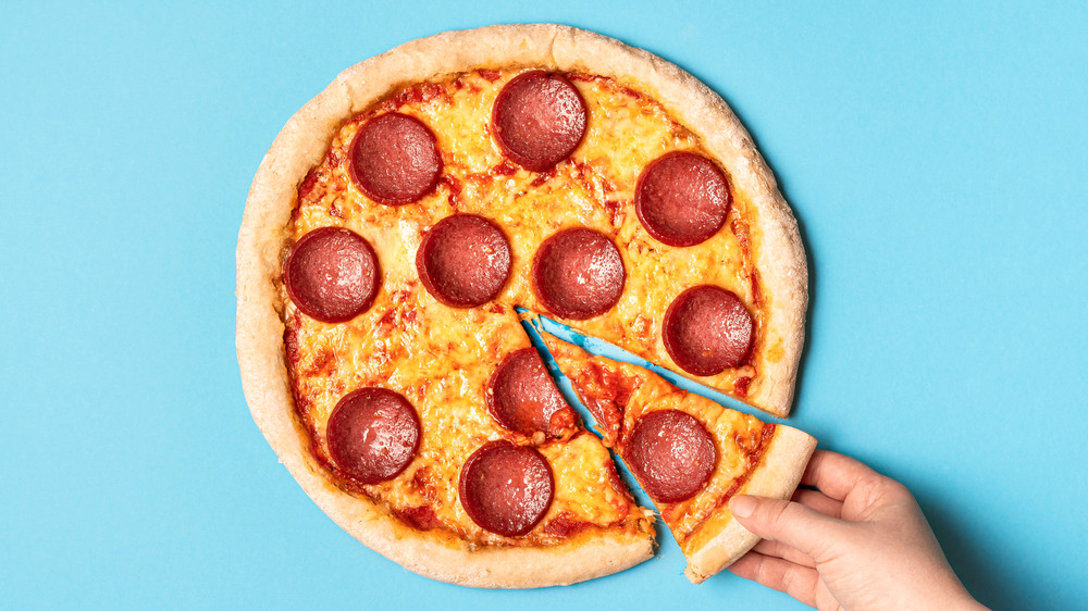 A sliced pizza against a plan backdrop as a hand removes one slice