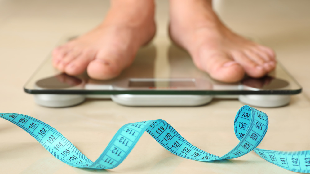 Person standing on scale with tape measure on floor