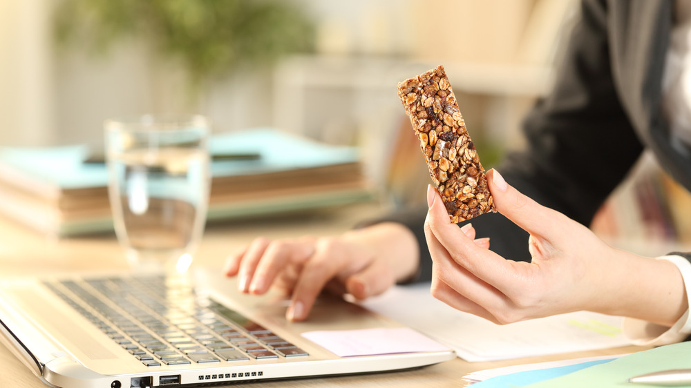 Image of woman working at computer with nut bar in hand