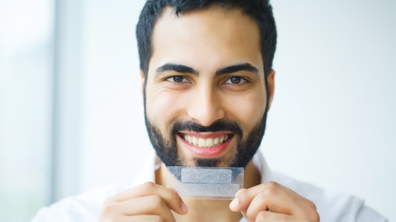man holds teeth whitening strip