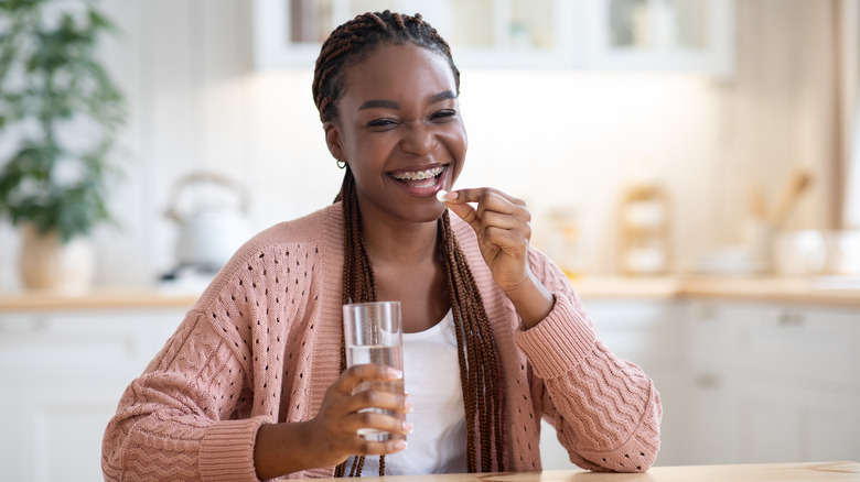 Woman smiling, holding vitamin