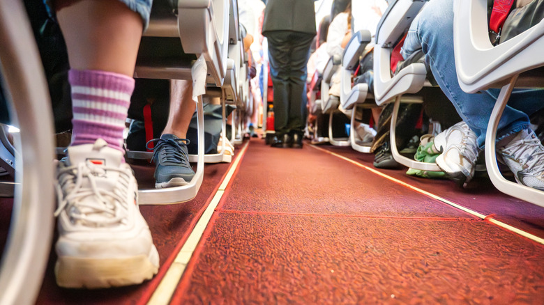 A low-angle shot of the aisle of an airplane with people wearing sneakers