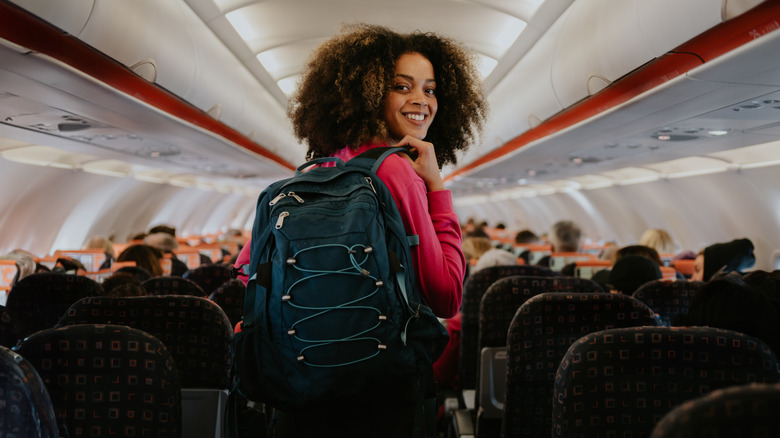 A woman smiling while carrying a backpack and walking down the aisle of an airplane