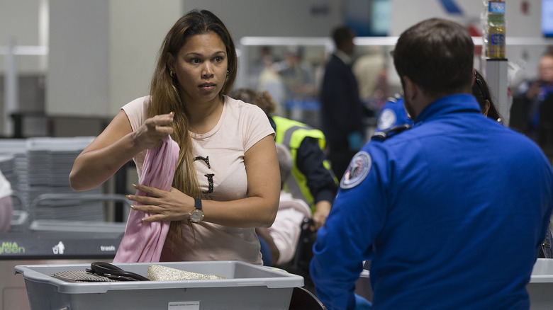A woman placing a pink sweater into a luggage bin on a TSA conveyor belt