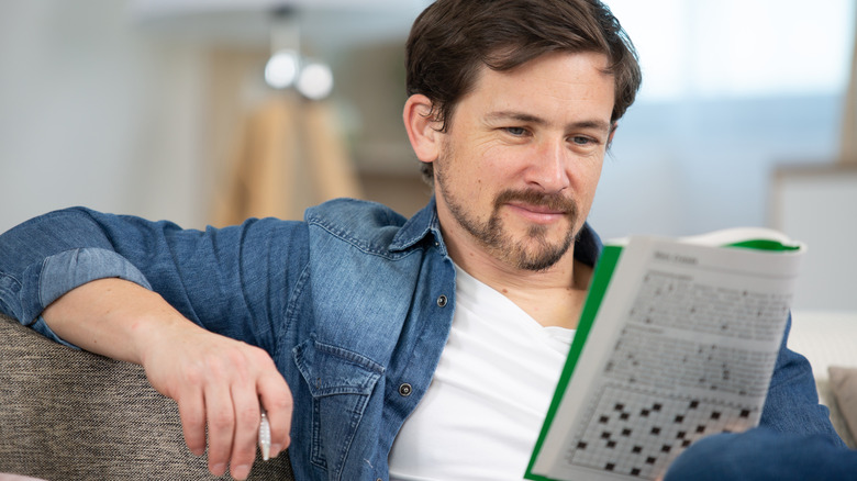 A man sitting on the couch doing a crossword puzzle