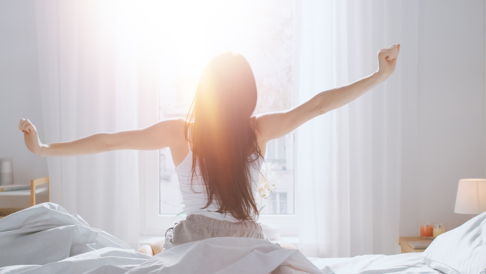 young woman yawning while getting out of bed 