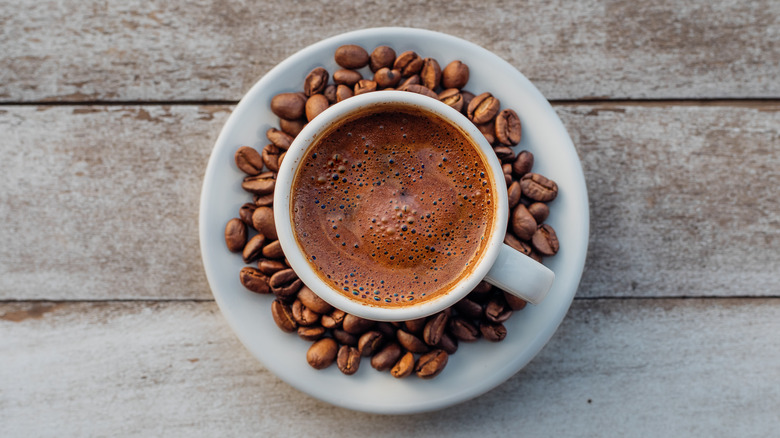White mug of Greek coffee surrounded by coffee beans on a saucer