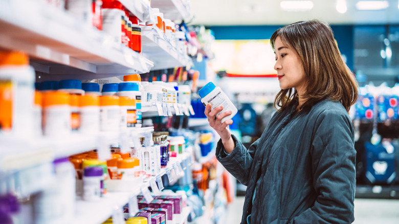 A woman looking at the label of a supplement bottle in a pharmacy aisle