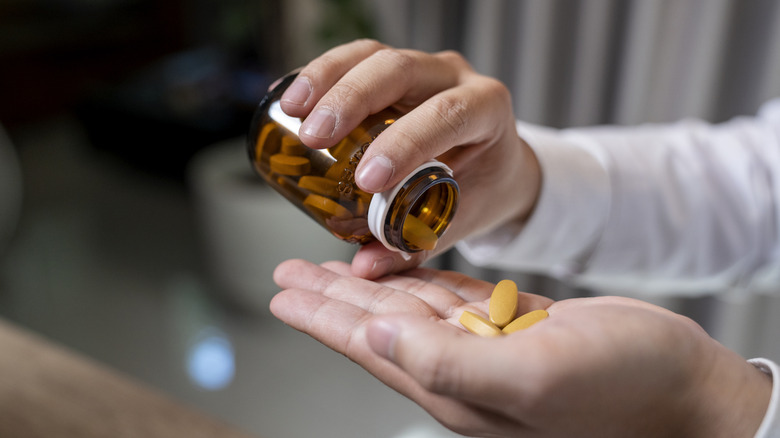 A man dispensing supplement tablets on his palm