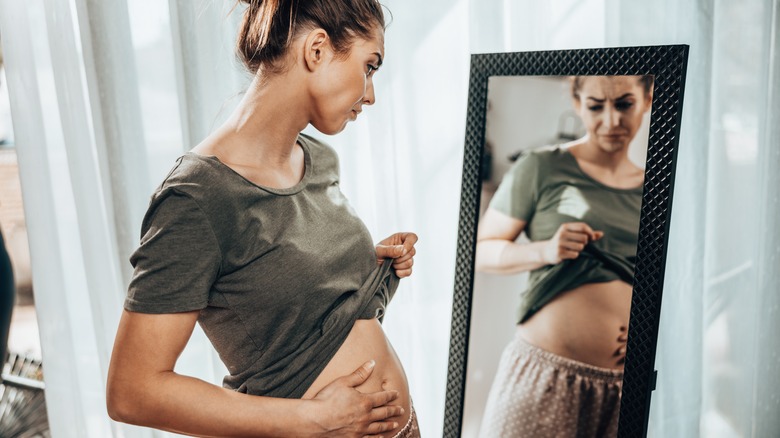 Women checking her belly in the mirror, feeling boated