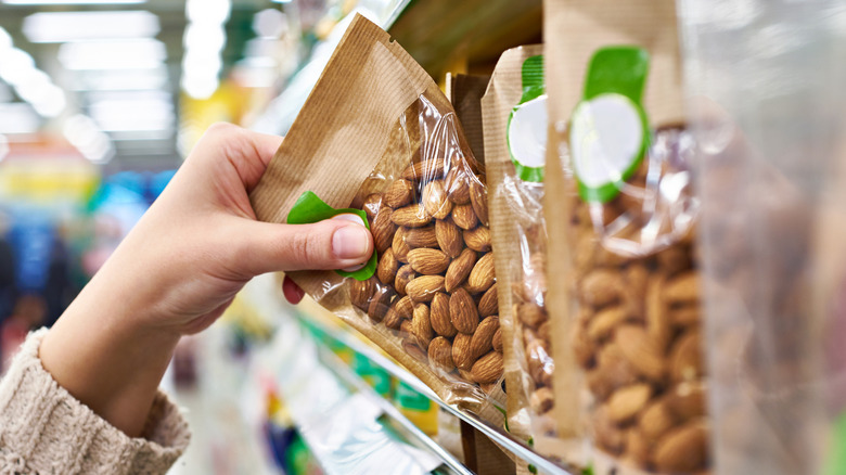 A hand reaching for almonds at a supermarket aisle