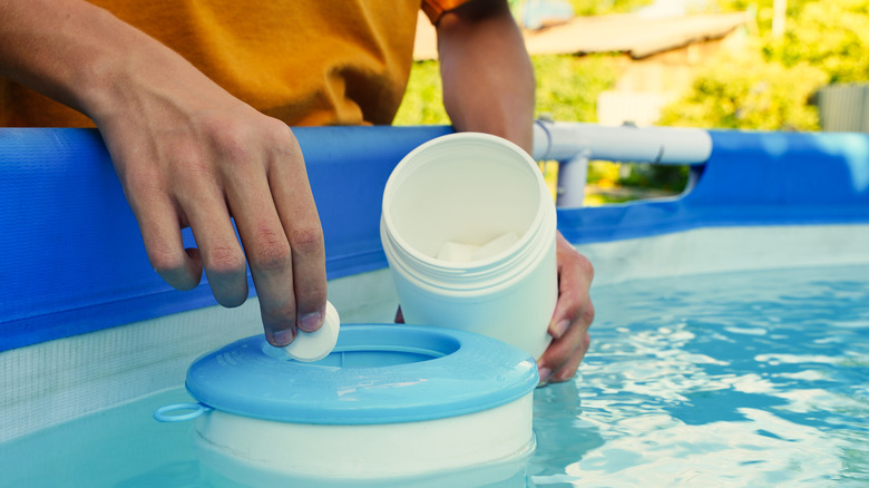 Hand dropping white chlorine tablets into outdoor swimming pool