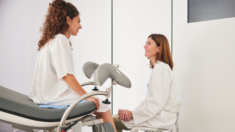 A woman seated on a medical examination table while gynecologist talks to her