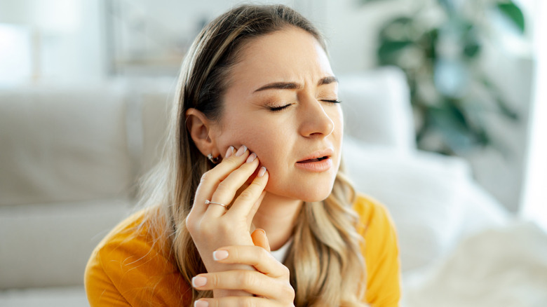 A woman with her eyes closed holding her painful jaw