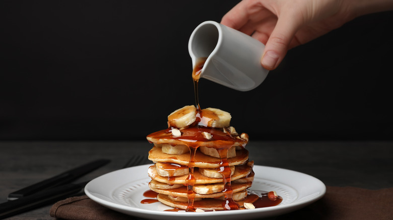 Person pouring maple syrup on stack of pancakes