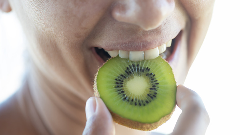 woman biting into a slice of kiwi fruit