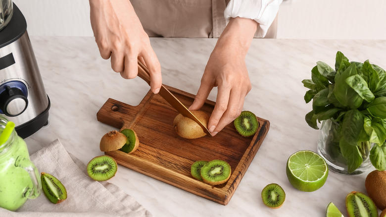 woman cutting kiwi on board in kitchen