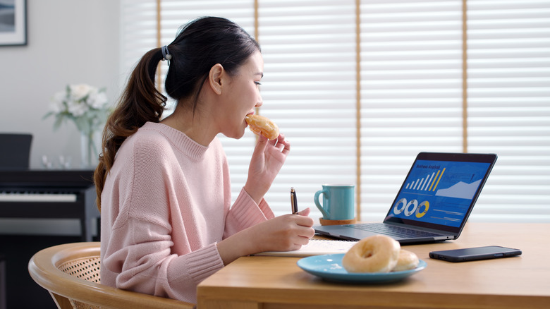 woman eating donut working computer