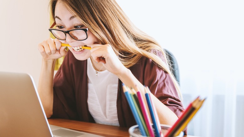 Woman biting pencil at computer