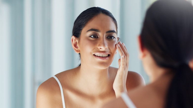 woman applying oil on her face in mirror