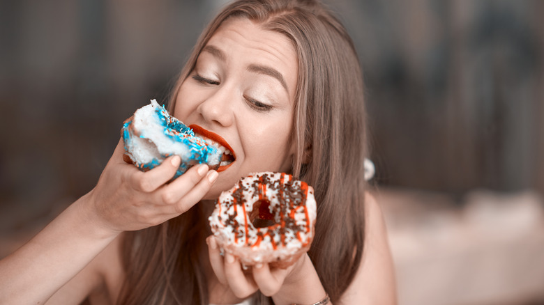 woman eating two sugary donuts
