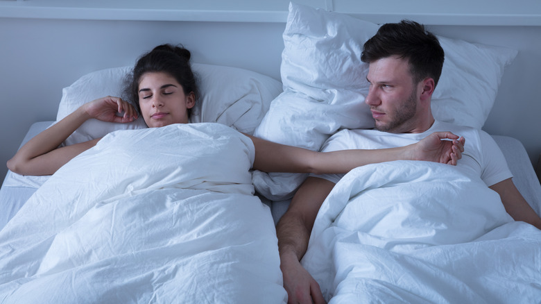 man glaring at sleeping woman beside him
