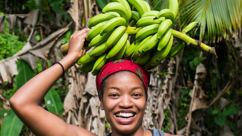 woman carrying bunch of green bananas