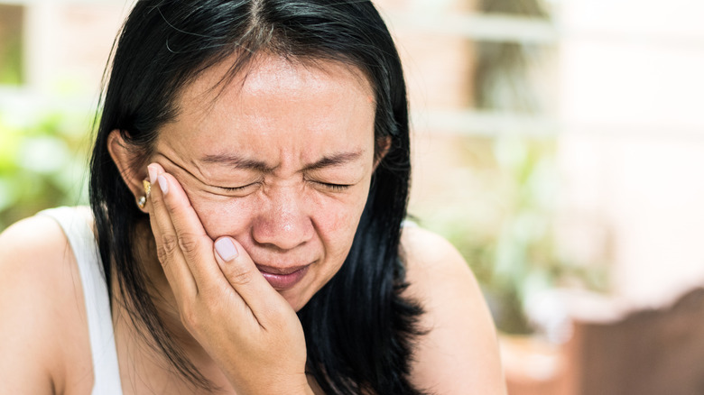 woman with hand on face wincing in pain