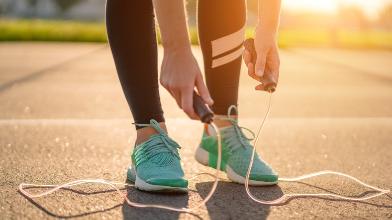 Close up of person wearing blue sneakers and black leggings with jump rope by feet