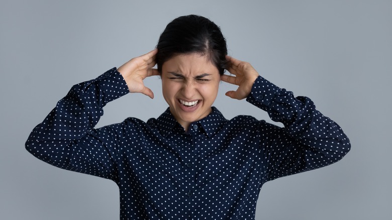 Woman wincing in pain covering her ears