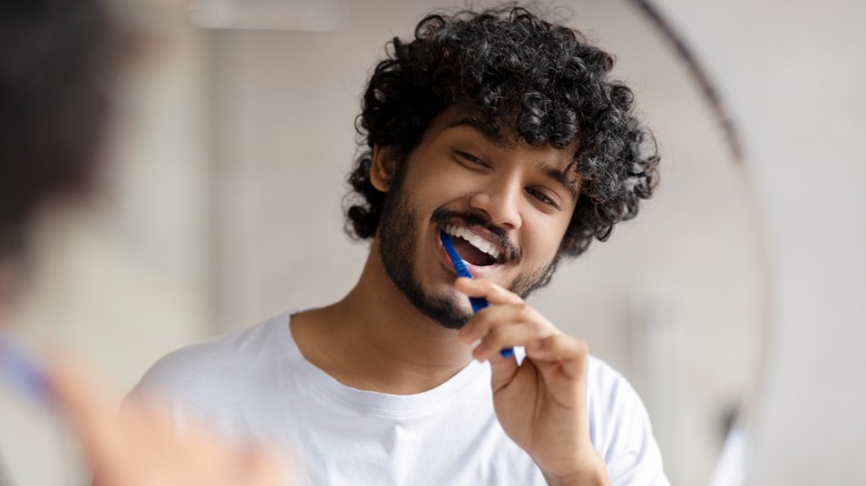 man brushing his teeth while looking in the mirror