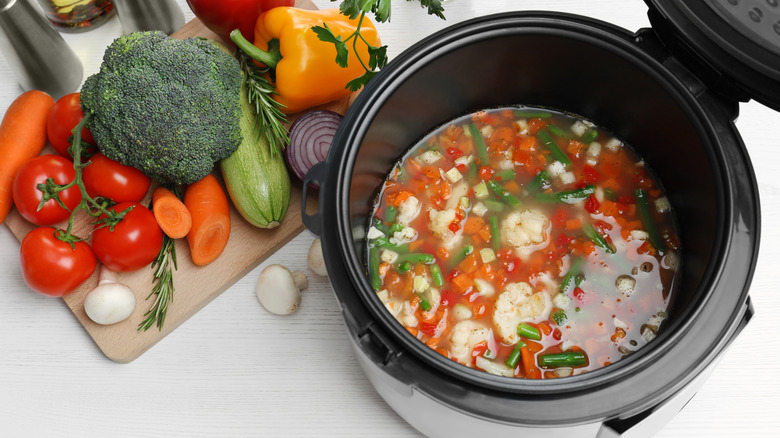 Crockpot filled with stew next to a collection of vegetables on a cutting board