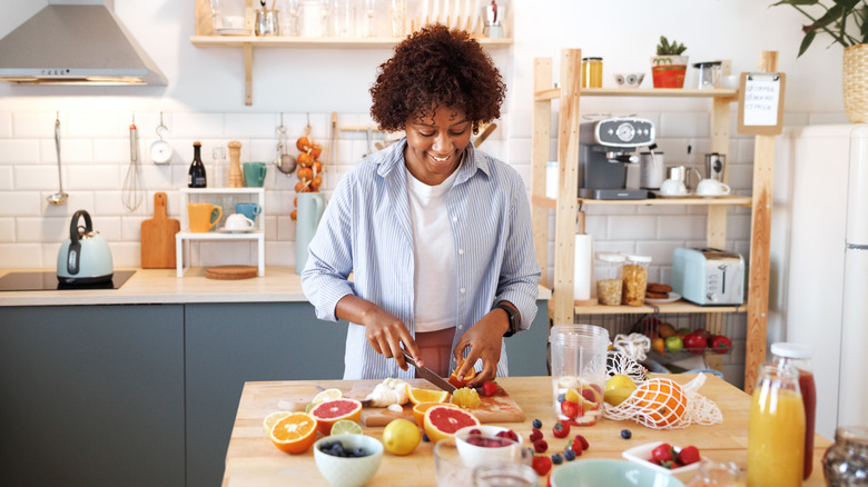 woman cutting up various citrus fruits for smoothie