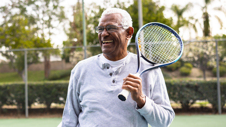 older man smiling while holding a tennis racket