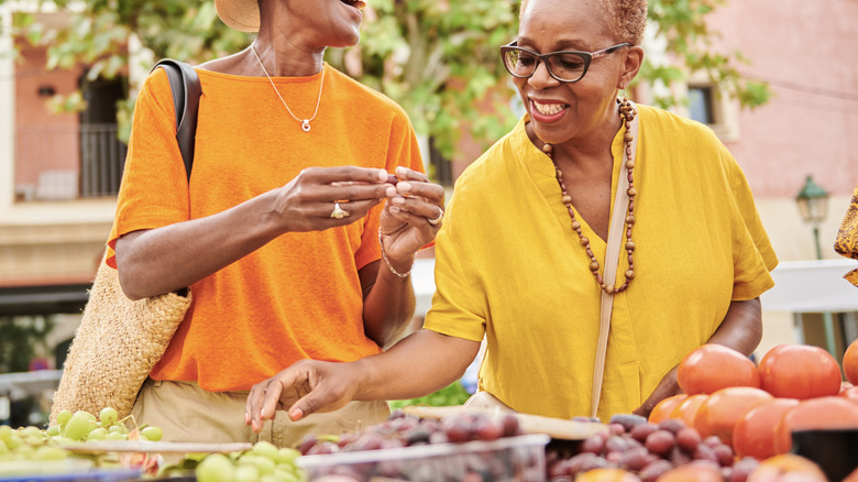 Two smiling women picking through produce at a farmers' market