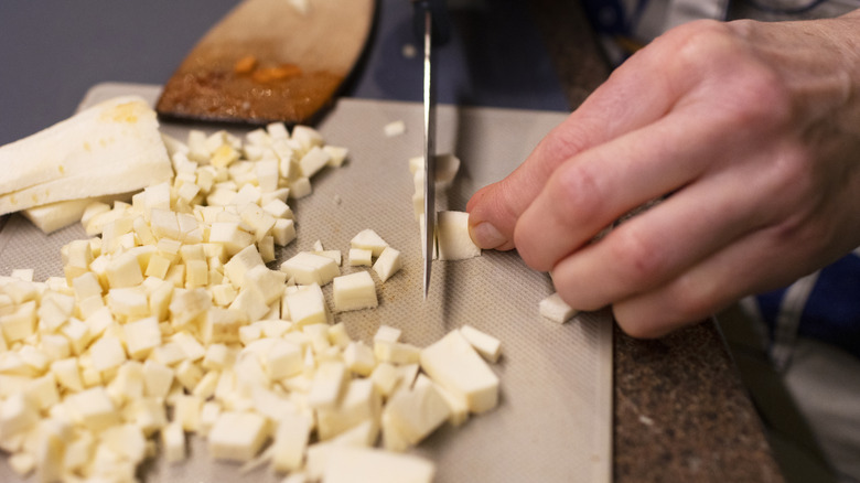 A close-up of a hand chopping parsnips