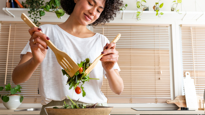 A woman tossing a salad in a large wood bowl