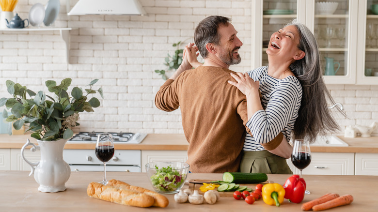 Happy middle-aged couple dancing together in the kitchen, preparing food