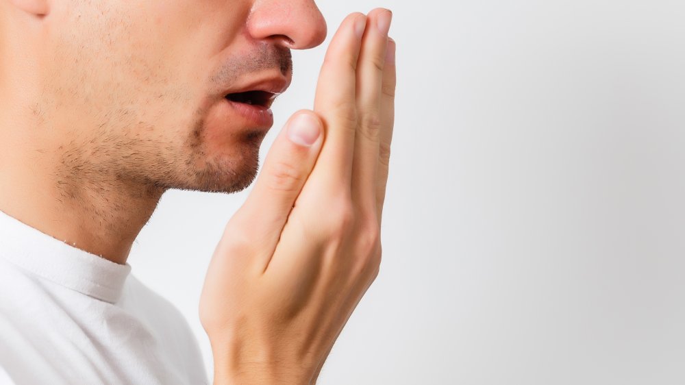 Man in white shirt checking his breath with his hand