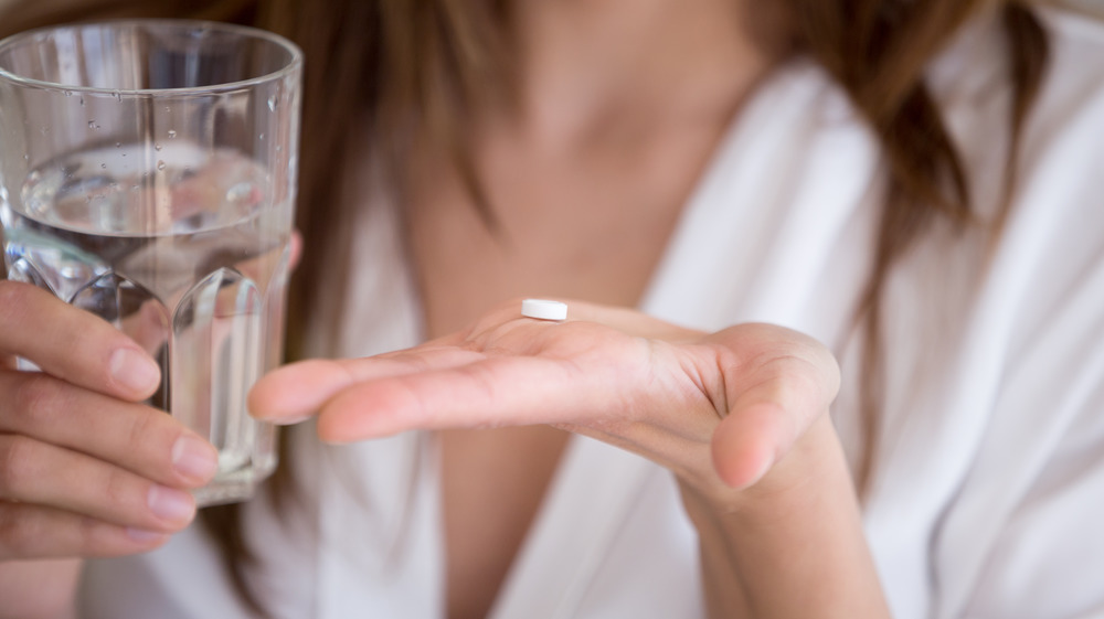 close up of a woman holding up a pill with a glass of water