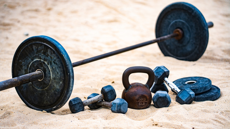 A barbell, dumbbells, and kettlebells on the sand
