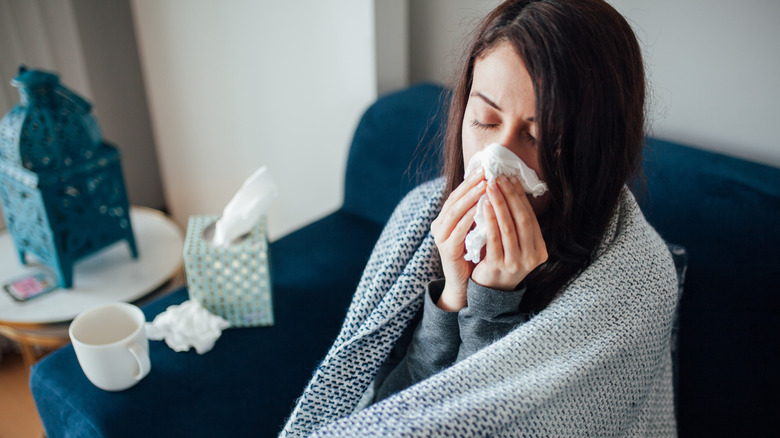 Woman wrapped in blanket blowing her nose