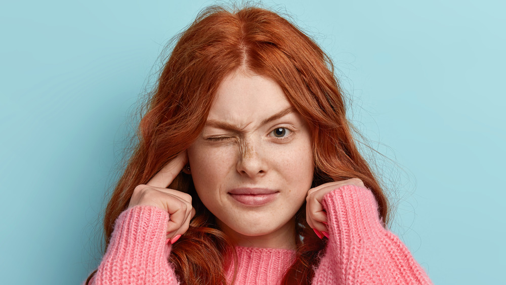 woman closing one eye, plugging ears