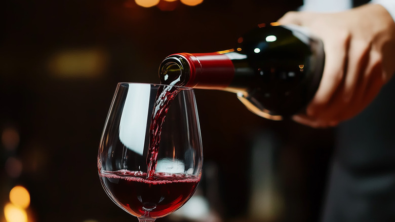 hand pouring bottle of red wine into a glass