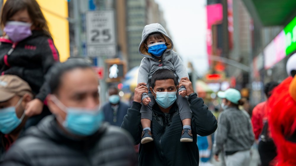 Man carries a child on his shoulders; both wear masks